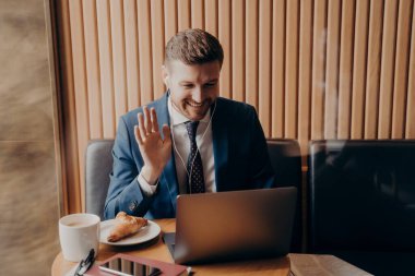 Erkek ofis çalışanı dizüstü bilgisayardan iş arkadaşlarına el sallıyor.