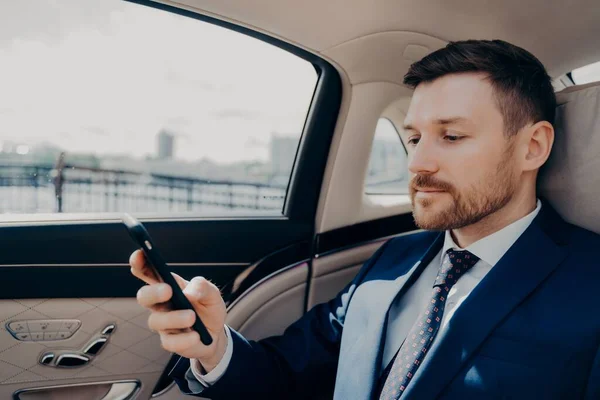 Инвестор проверяет телефон во время езды в лимузине — стоковое фото