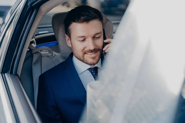 Businessman rides in black car in passenger seat and talking on cellphone