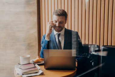 İş adamı telefonda konuşuyor ve kafede dizüstü bilgisayarla çalışıyor.