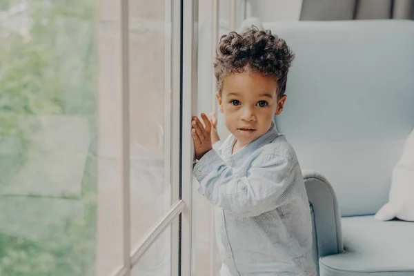Retrato de lindo bebé de pelo rizado de raza mixta esperando a los padres cerca de la ventana — Foto de Stock