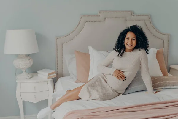 Felice donna africana americana incinta che riposa sul letto in appartamento moderno — Foto Stock