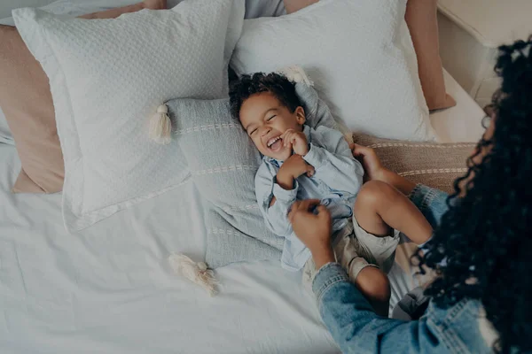 Preciosa madre cosquillas su lindo hijo pequeño acostado en la cama y riendo — Foto de Stock