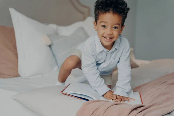 Адекватний маленький афро-американець усміхається дитині в блакитній сорочці, граючи на батьківській ліжку. — стокове фото