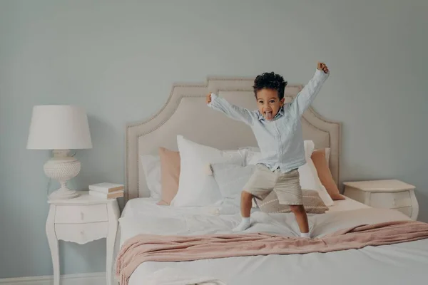 Adorable lindo niño saltando alegremente en la cama y divertirse en casa — Foto de Stock