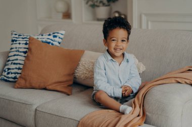 Tatlı afro çocuk rahat bir koltukta oturup içeride oynuyor.