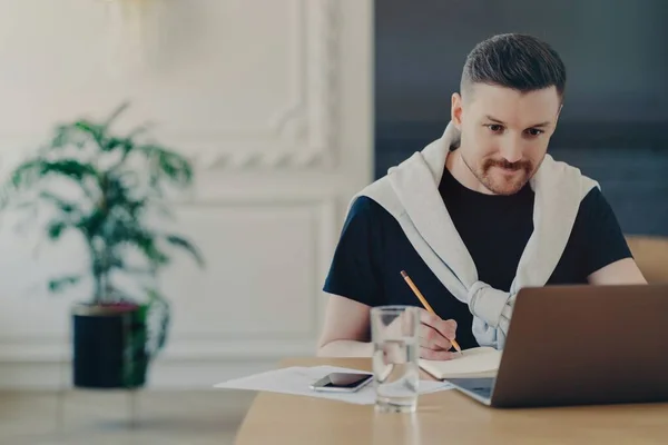 Uomo impiegato guardando il computer portatile e prendendo appunti mentre seduto in ufficio — Foto Stock