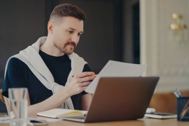 Konsantre adam kağıt belgelerden bilgi ya da verileri okur. Masaüstü pozlarında rahat iç mekanlara karşı çalışır. Çalışmakla meşgul gibi giyinir. Ortak çalışma alanında erkek girişimci