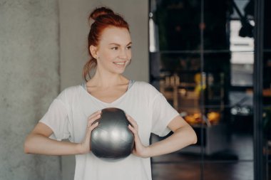 Kırmızı saçlı, sportif, pozitif kadın mini egzersiz topu tutuyor.