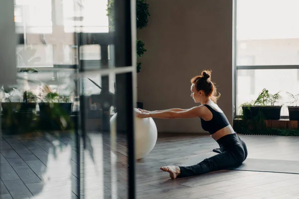 Giovane rossa donna snella seduta in spago con fitball, facendo esercizi di stretching — Foto Stock