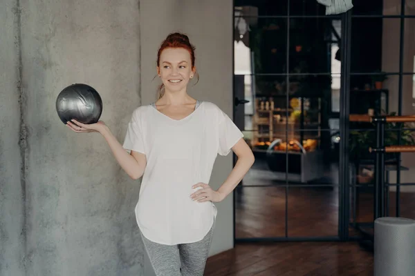Κοκκινομάλλα ευτυχισμένη γυναίκα στέκεται στο γυμναστήριο με μικρή ασημένια μπάλα — Φωτογραφία Αρχείου