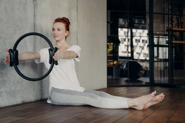 Giovane donna rossa concentrata che fa esercizi di forza con anello pilates — Foto Stock