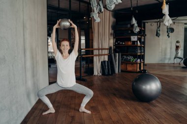 Aktif durumdaki mutlu sporcu kadın, mini fitball 'u kafasının üstünde yarı konumda tutuyor.