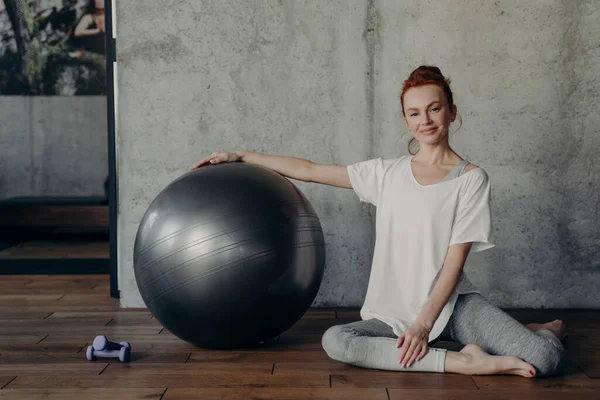 Felice giovane donna fitness rilassante dopo l'allenamento di pilates mentre seduto con grande palla esercizio sul pavimento — Foto Stock