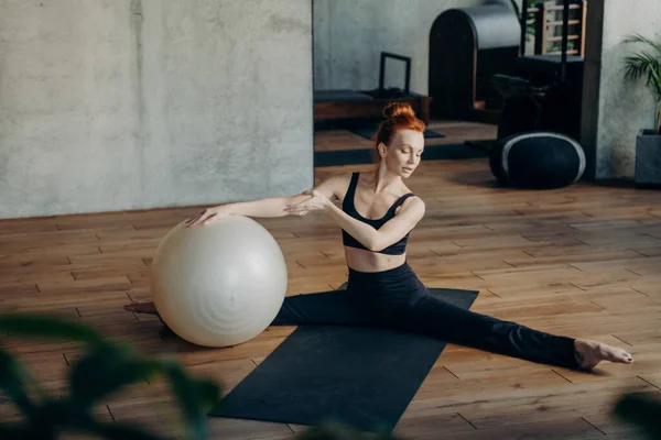 Giovane donna in posizione divisa che si esercita con fitball in palestra — Foto Stock