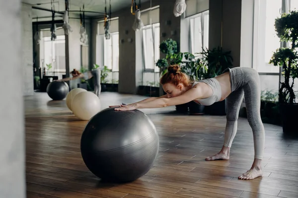 Karcsú nő nyújtózkodik vissza a gyakorló labdát, miközben dolgozik ki a modern fitness stúdió — Stock Fotó