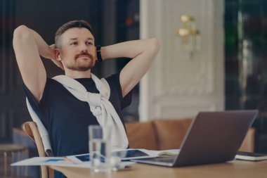 Düşünceli sakallı adam görevinin başında el ele tutuşup modern aletlerle masanın başına oturur. Mesafeli işi düşünür. Omuzlarının üzerine kazak bağlanmış tişört giyer.