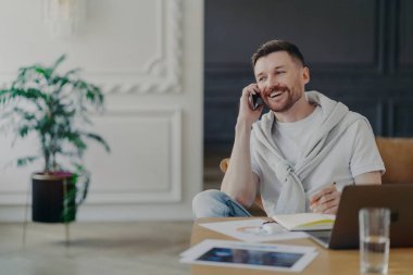 Ev ofisinin çalışma masasında oturup telefonla konuşan mutlu bir serbest yazar.