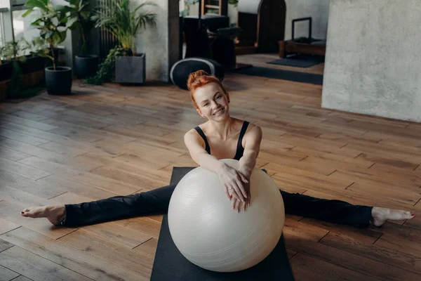 Sorridente zenzero donna sana in posizione divisa che si estende con fitball — Foto Stock