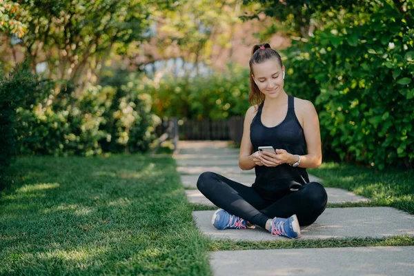 Mulher esportiva tem pausa para refresco verifica mensagens e notificação compartilha conteúdo sobre fitness ao ar livre vestida com desgaste ativo leva a relaxamentos estilo de vida saudável após treinamento cardio ativo — Fotografia de Stock