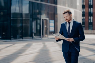 Ofis binasının yanında yürürken gazete okuyan resmi giyinmiş bir iş adamı.
