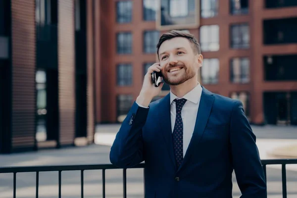Férfi irodai dolgozó élvezi a kellemes beszélgetést telefonon, miközben az irodaház mellett áll a szabadban — Stock Fotó