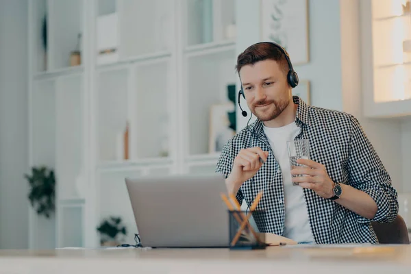 Concept d'éducation et d'apprentissage en ligne. Satisfait homme occupé concentré à l'affichage de l'ordinateur portable montre webinaire éducatif écoute cours audio via écouteurs assis sur le bureau bénéficie d'études virtuelles avec tuteur — Photo