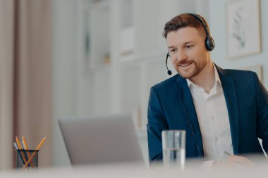 Gülümseyen genç adam evdeki online toplantı sırasında iş arkadaşıyla konuşuyor.