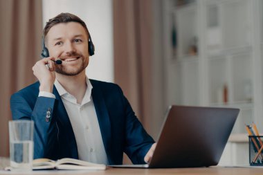 Kulaklıklı, dizüstü bilgisayar kullanan yakışıklı genç adam.