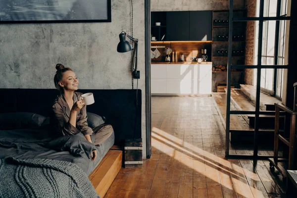 Jovem menina atraente feliz sentado na cama em posição de lótus e beber café da manhã — Fotografia de Stock