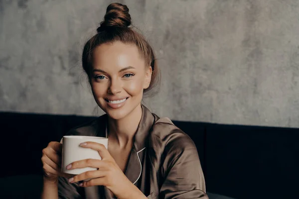 Retrato de jovem mulher morena atraente com belo sorriso largo bebendo café na cama — Fotografia de Stock