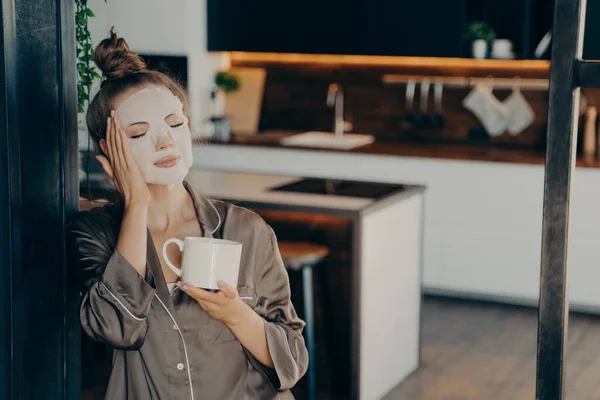 Mujer joven en pijama de seda que se queda en casa y disfruta de una taza de café por la mañana — Foto de Stock