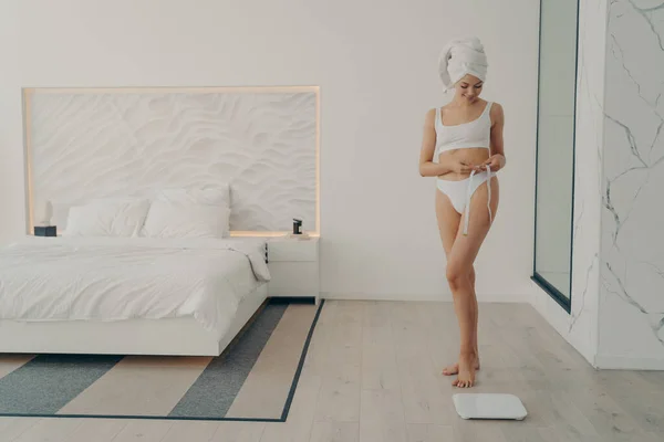 Όμορφη λεπτή εφαρμογή γυναικείο μοντέλο ποζάρουν σε λευκό εσώρουχο με ταινία μέτρησης στο χέρι — Φωτογραφία Αρχείου