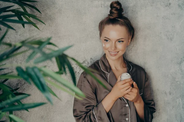 Jonge blanke aantrekkelijke vrouw in zijde bruine pyjama doet huidverzorging procedure thuis — Stockfoto