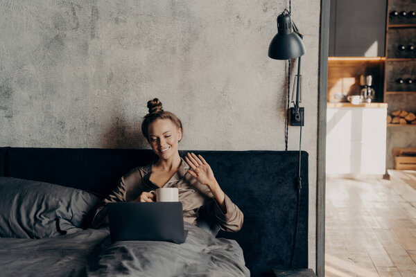 Relaxed calm young girl lying down on bed and chatting online with her friends on laptop