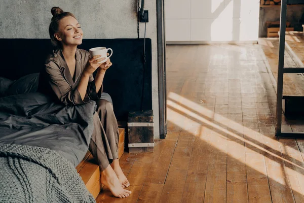 Schattig mooi meisje met kopje koffie chillen in de ochtend terwijl zitten op bed — Stockfoto