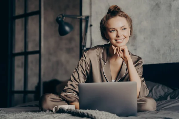 Retrato de bela mulher de negócios pensativamente sorridente em pijama de cetim trabalhando remotamente de casa de manhã — Fotografia de Stock