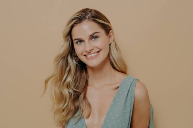 Uzun sarı saçlı bir kadın model kameraya mutlu ve pozitif bir ifadeyle bakıyor.