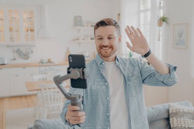 Oturma odasında akıllı telefondan selfie çeken yakışıklı adamın fotoğrafı.