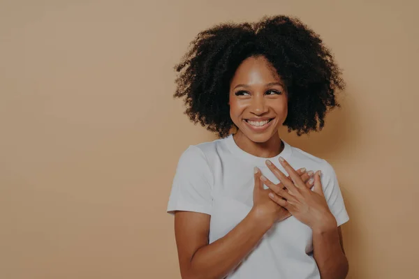 Portrait of happy african woman posing with smile looking away, holding hands on chest — Stock Photo, Image