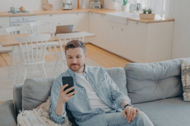 Evde akıllı telefon kullanan, günlük kıyafetlerle çekici beyaz bir genç adam.