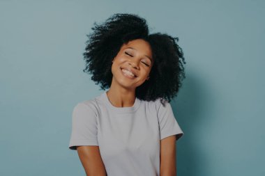 Pastel mavi stüdyo arka planında izole edilmiş afro saç stili olan neşeli genç kadın portresi.
