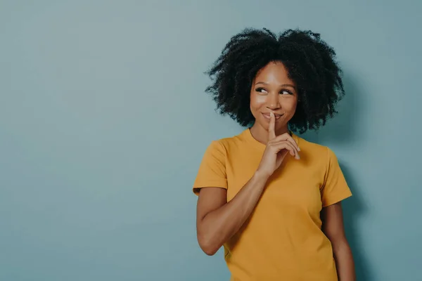 Cheerful afro girl showing shhh sign with finger near lips, standing over pastel blue background — Φωτογραφία Αρχείου