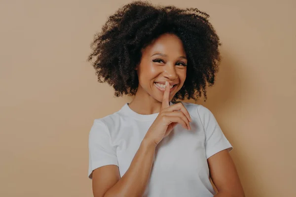 Cheerful smiling afro girl showing shhh sign, keep silence gesture, with index finger near lips — Foto de Stock