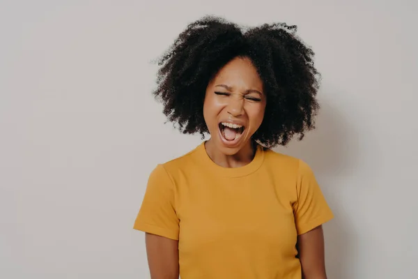 Jeune belle femme africaine aux cheveux bouclés portant un t-shirt jaune décontracté criant de colère — Photo