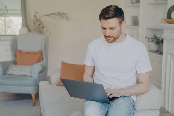 Sérieux jeune homme utilisant un ordinateur portable pour le travail à distance de la maison — Photo