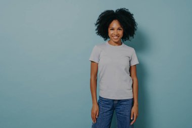 Keyifli genç Afrikalı kadın mavi arka planda yalnız poz veriyor.