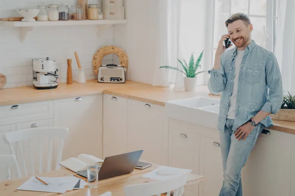 Szczęśliwy młody biały człowiek mając rozmowa na telefon komórkowy w kuchnia — Zdjęcie stockowe