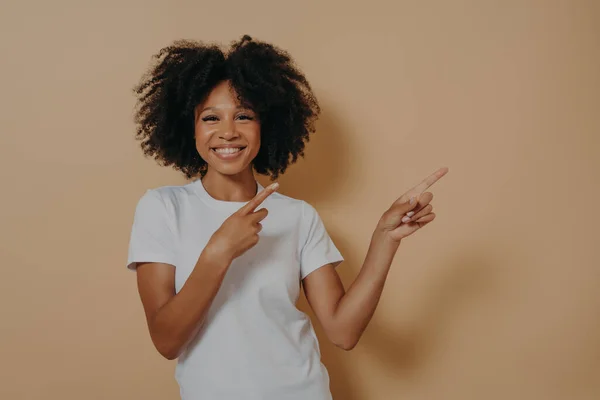 Позитивна весела темношкіра жінка вказує на місце для копіювання ізольовано на бежевому фоні — стокове фото