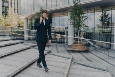 Ofis merkezinde yürürken akıllı telefondan konuşan Kafkasyalı mutlu iş adamı.